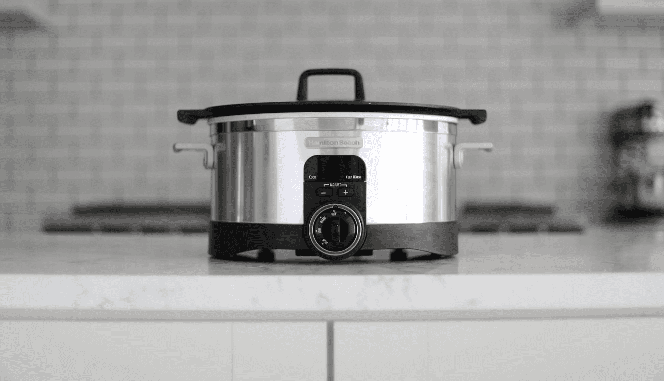 A stainless steel slow cooker with a black lid on a kitchen counter.